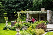 Eine Gruppe sitzt am Tisch in sommerlichem Garten unter der Pergola