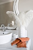 White ostrich feathers in elegant porcelain vase on vintage washstand with vanity mirror