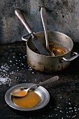 Selbstgemachte Karamellsauce auf Teller mit Löffel, verstreuter Zucker und alter Kochtopf