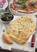 Pizza bread with rosemary and olives with a pizza in the background
