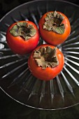 Three persimmon on a glass stand