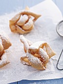 Crispy fried pasty with icing sugar on a piece of baking paper