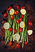 Asparagus, lemon slices and organic grape tomatoes with olive oil and spices on a baking tray