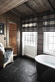 Badezimmer mit schwarzem Schieferboden, an Sprossentür und Fenster Raffrollos mit Karomuster, im Hintergrund Blick in die Sauna