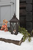 Straw animal figurine next to lit candle in floor lantern on snowy step