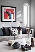 Lit candles in candelabra and tealight holder on table, scatter cushions on sofa below modern artwork on grey wall in traditional interior