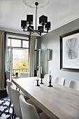 Lit candles in candlesticks on wooden table below pendant lamp with black lampshades in front of open balcony door