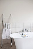 Free-standing bathtub next to stainless steel ladder-style towel rack