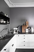 L-shaped kitchen counter with dark stone counter and white base units below grey wall and stucco ceiling