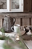 Thermos jug with wicker cover and coffee cup on white chip wood tray on festively decorated table