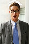 Mann mit Brille, grauem Sakko und Krawatte schneidet Grimassen: überrascht oder verblüfft