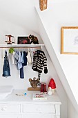 Shelf and child's clothing on clothes rail above white-painted vintage changing cabinet in attic room