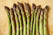 A row of green asparagus spears on a wooden board