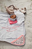 Pale grey picnic blanket with crocheted trim and seagull motif on sand