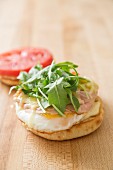 An English muffin with eggs, cheese, ham rocket and tomatoes for breakfast