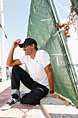 Man wearing a T-shirt, sunglasses and a baseball cap sitting on the side of the road