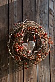 Wreath of berries, branches and rose hips with wooden love-heart in centre hung on wooden wall