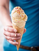 A hand holding a cone of vanilla ice cream