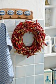 Kranz aus getrockneten roten Chilischoten, an Wandhakenleiste in Küche aufgehängt