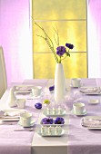 Table set for Easter meal with white crockery and pale lilac tablecloth