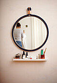 Round wall mirror with rope frame above floating shelf in bathroom