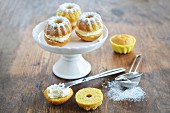 A mini Bundt cake with cream and icing sugar on a cake stand