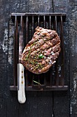 Grilled peppered steak on a grill rack with a knife