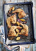 Roast chicken legs with lemons and red onions on a baking tray