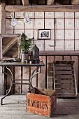 Old wooden crate in front of metal-framed side table and checked wallpaper in rustic attic interior