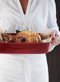 A woman holding a roast pork roulade in a roasting dish