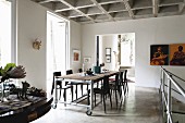 Dining table on castors with dark chairs opposite landing balustrade on open-plan gallery below concrete coffered ceiling