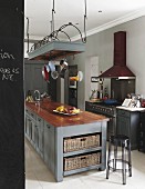 Grey-painted island counter below suspended wire rack of cooking utensils and transparent bar stool in kitchen