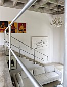 View from gallery of masonry staircase with metal balustrade of white sofa in open-plan interior with concrete coffered ceiling