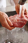 A piece of meat being rinsed under cold running water