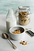 A bowl of muesli with a bottle of milk and a jar of muesli in the background