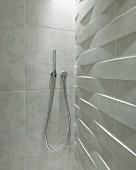 Moderne, stabförmige Handbrause auf Fliesen mit marmorierter Oberfläche in Duschkabine