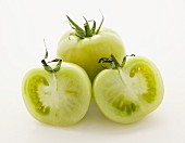 Grüne Tomaten, ganz & halbiert vor weißem Hintergrund