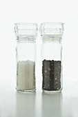 Salt and pepper in Plexiglass mills on a white surface