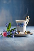 A steaming cup of coffee with a small bouquet of forget-me-nots and daisies