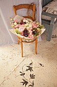 Holzstuhl mit Blumenstrauss in der Sitzfläche, davor auf Bodenmalerei mit floralem Motiv