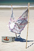 Hammock attached to sticks stuck in sandy beach next to picnic basket