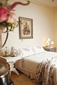 Romantisch nostalgisches Schlafzimmer mit geblümter Bettwäsche, Heiligenbild und Dekoobjekten unter Glasglocken