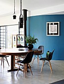 Klassiker Schalenstühle um ovalen Holztisch vor gebogener, blauer Wand