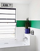 Bathtub below tilt window in white bathroom with green stripe along walls