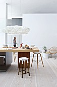 Barhocker um Küchentheke unter Designer-Pendelleuchte, in modernem, offenem Ambiente mit hellem Dielenboden