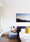 Schlafzimmer mit Doppelbett, gelbem Kissen und Berglandschaft auf Wandbild