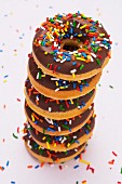 A stack of chocolate-glazed doughnuts with colourful sugar sprinkles