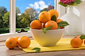 A bowl of mandarins on a table by a window