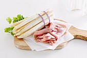 A bunch of white asparagus and ham on a chopping board
