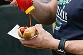 A man pouring ketchup onto a hot dog